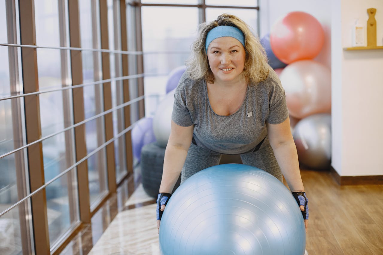 An adult woman engaging in a fitness workout with an exercise ball in a gym setting.